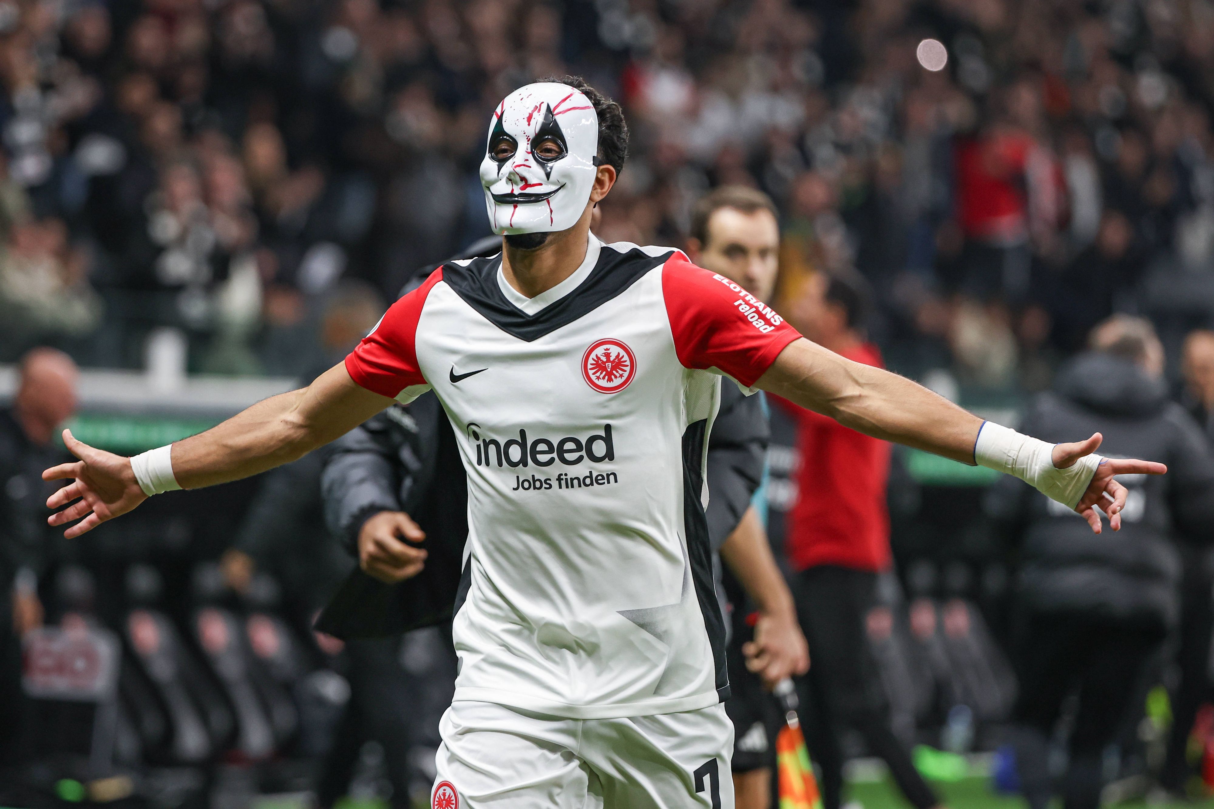 Omar Marmoush feiert mit einer Horror-Maske und ausgebreiteten Armen.