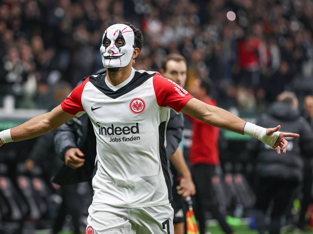Omar Marmoush feiert mit einer Horror-Maske und ausgebreiteten Armen.