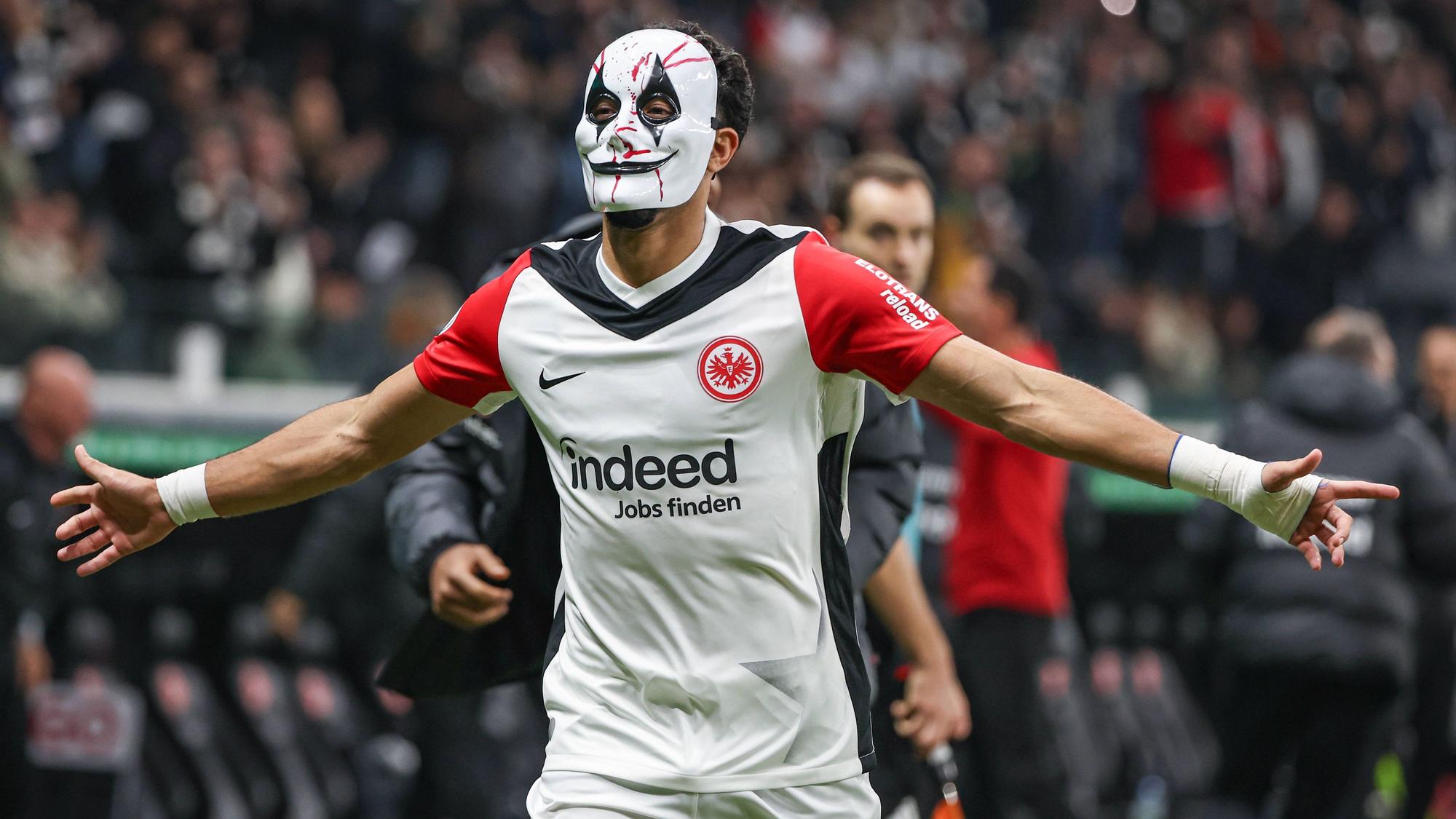 Omar Marmoush feiert mit einer Horror-Maske und ausgebreiteten Armen.
