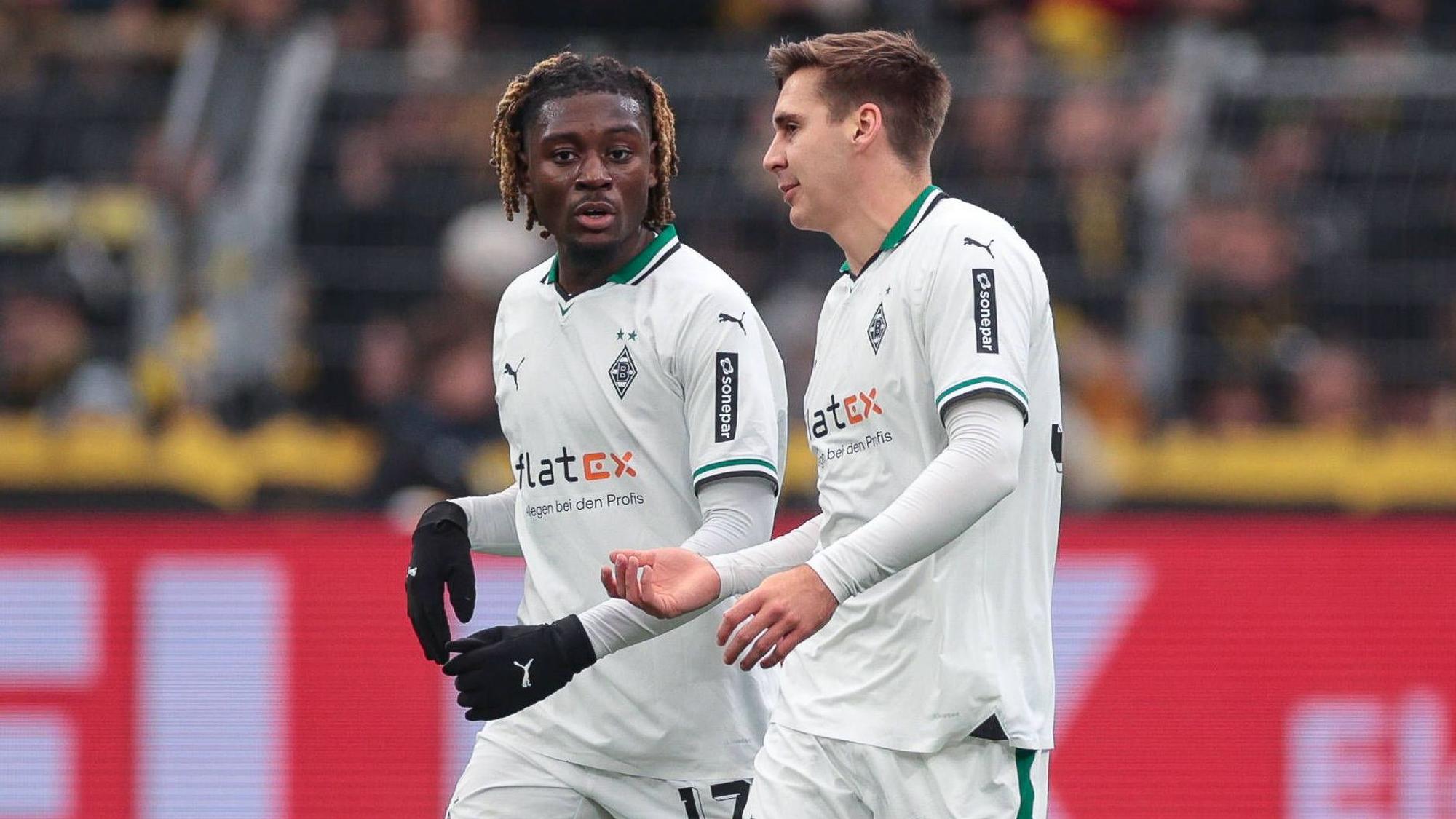 Die Gladbach-Profis Manu Koné und Maximilian Wöber laufen beim Spiel in Dortmund nebeneinander über den Rasen und unterhalten sich.