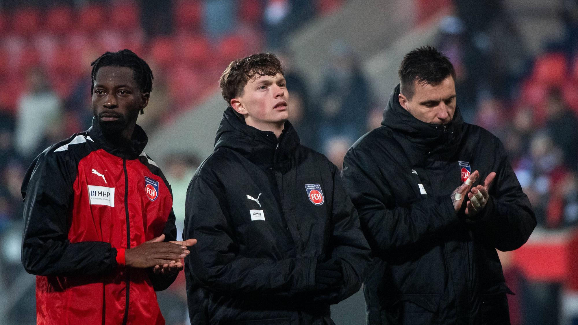 Die Heidenheim-Profis Omar Traoré, Paul Wanner und Kevin Müller stehen nach dem Playoff-Rückspiel in der Conference League gegen den FC Kopenhagen enttäuscht vor der Kurve und applaudieren den Fans.