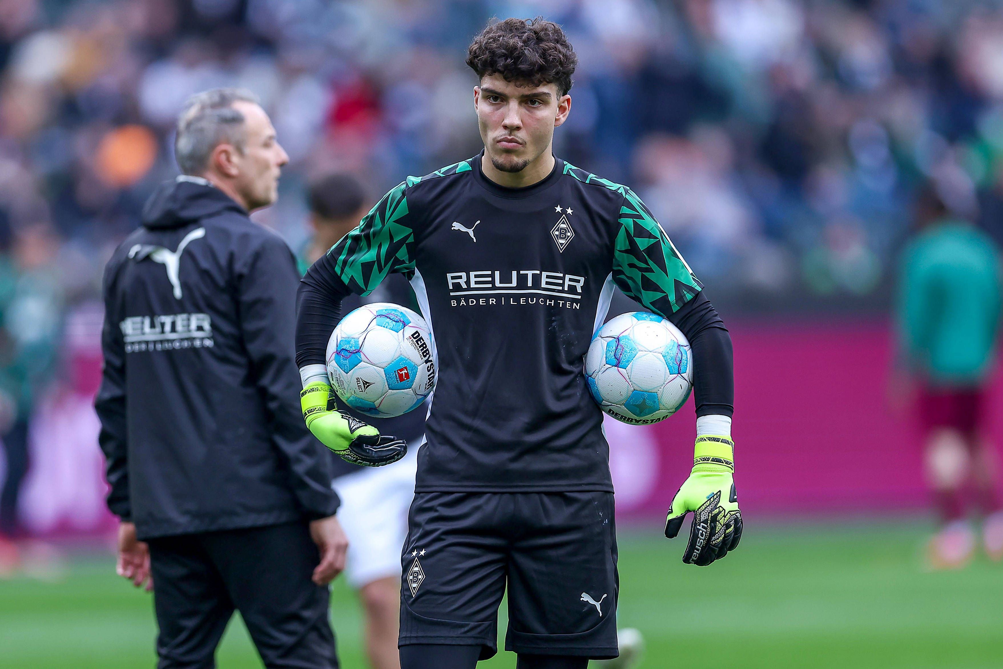 Borussia Mönchengladbachs Torwart Tiago Pereira Cardoso steht vor dem Bundesliga-Spiel gegen den FC Augsburg auf dem Platz und hält links und rechts zwei Bälle unter dem Arm.
