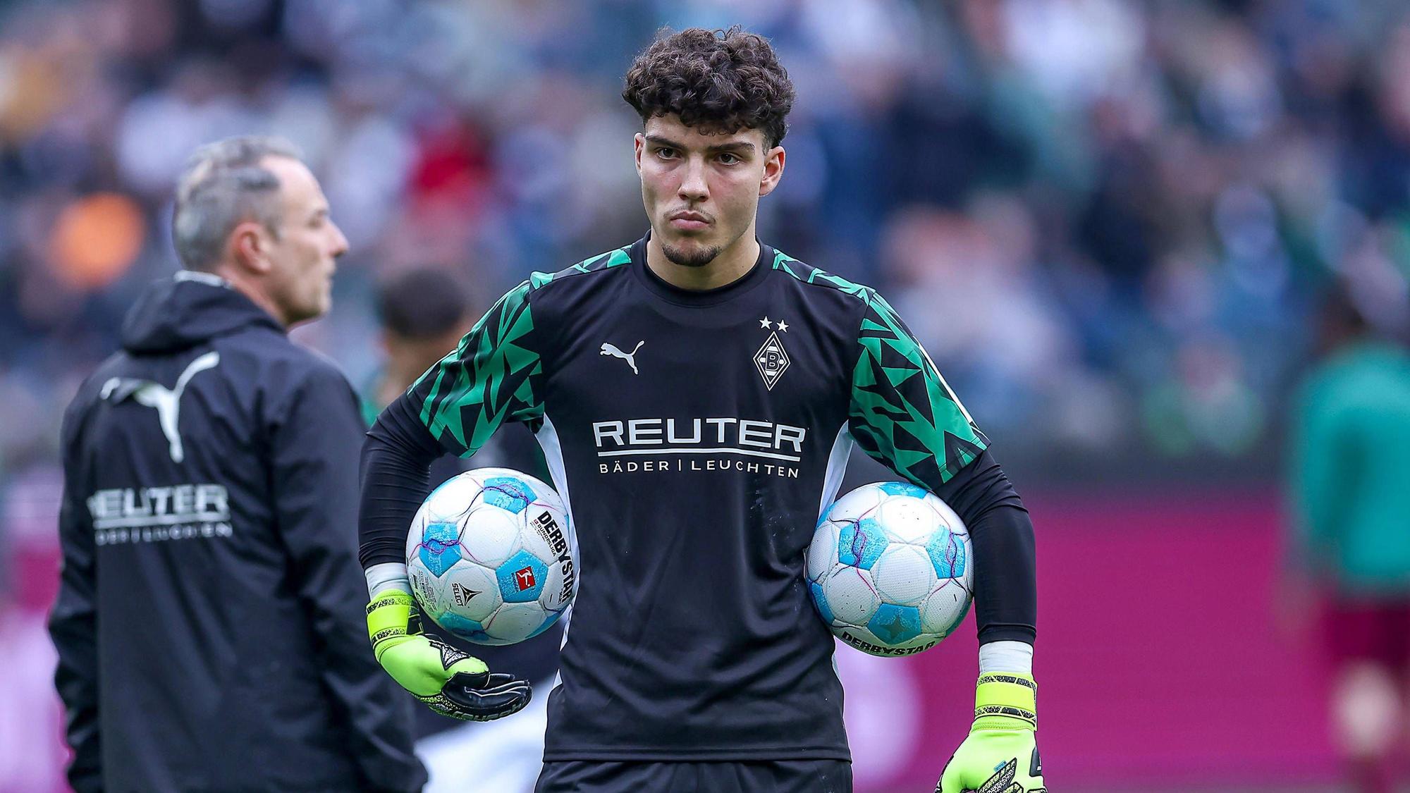 Borussia Mönchengladbachs Torwart Tiago Pereira Cardoso steht vor dem Bundesliga-Spiel gegen den FC Augsburg auf dem Platz und hält links und rechts zwei Bälle unter dem Arm.