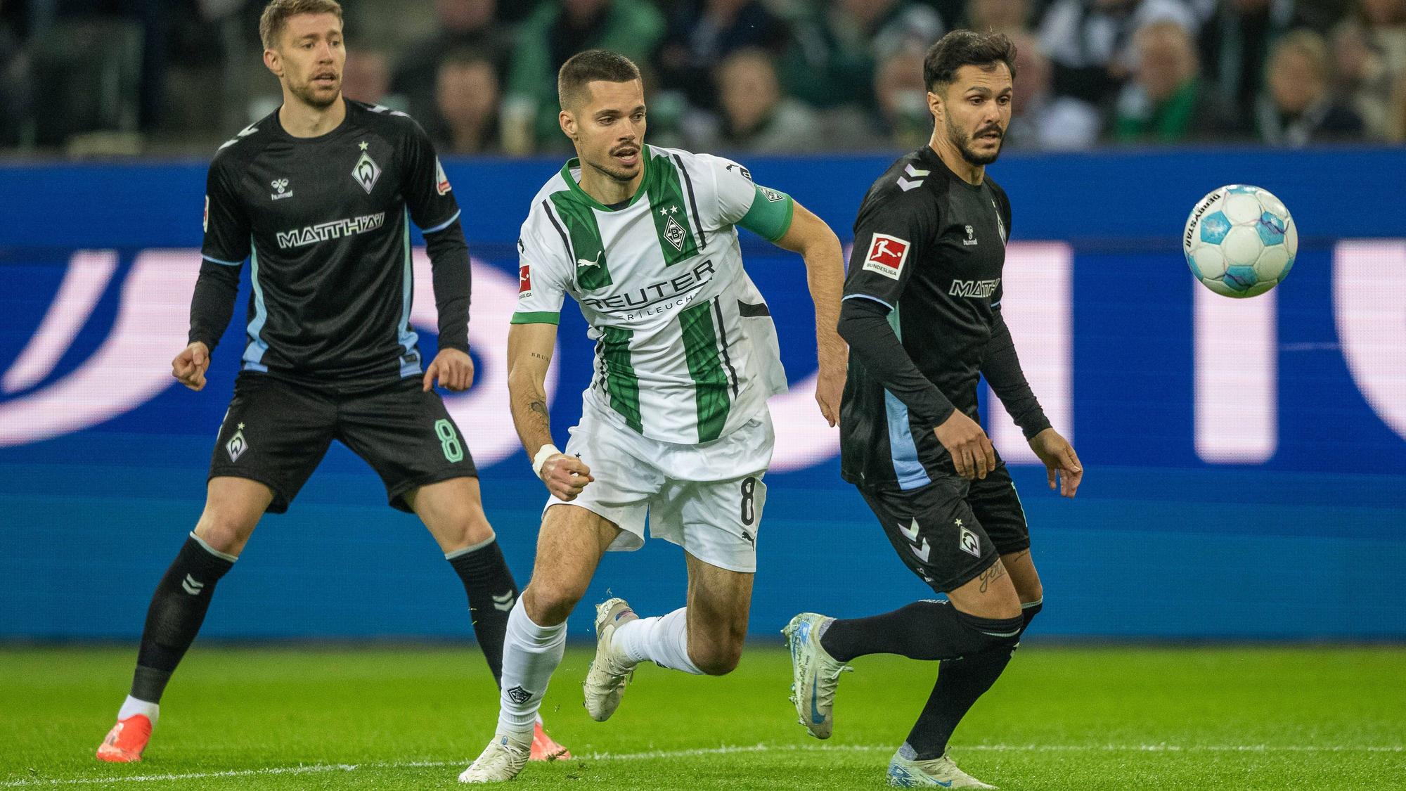 Borussia Mönchengladbachs Julian Weigl steht hinter Bremens Leonardo Bittencourt und hat den Ball im Blick, im Hintergrund beobachtet Werders Mitchell Weiser die Szene.
