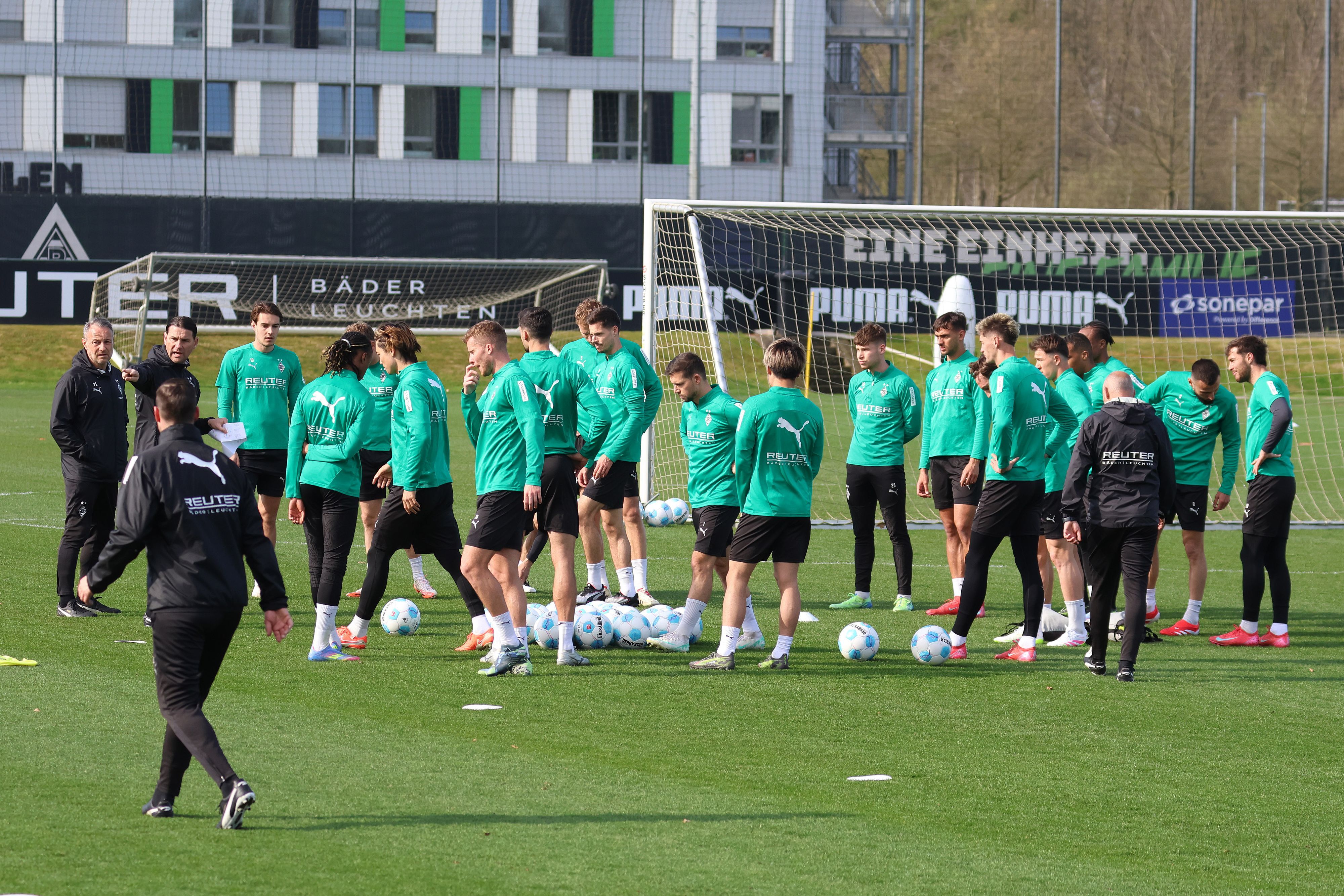 Die Gladbach-Profis und das Trainerteam auf dem Platz zum Training in der Sonne.