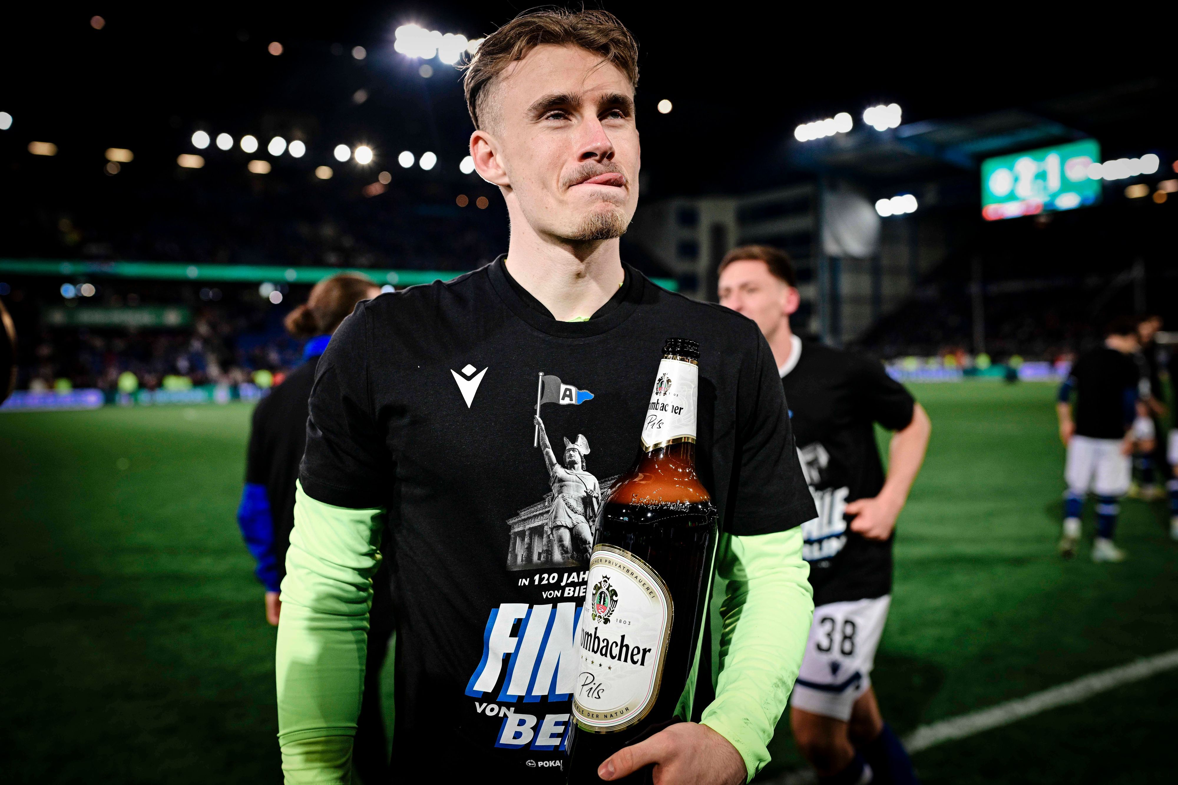 Jonas Kersken mit einer riesigen Flasche Bier in der Hand. Er leckt sich die Lippen.