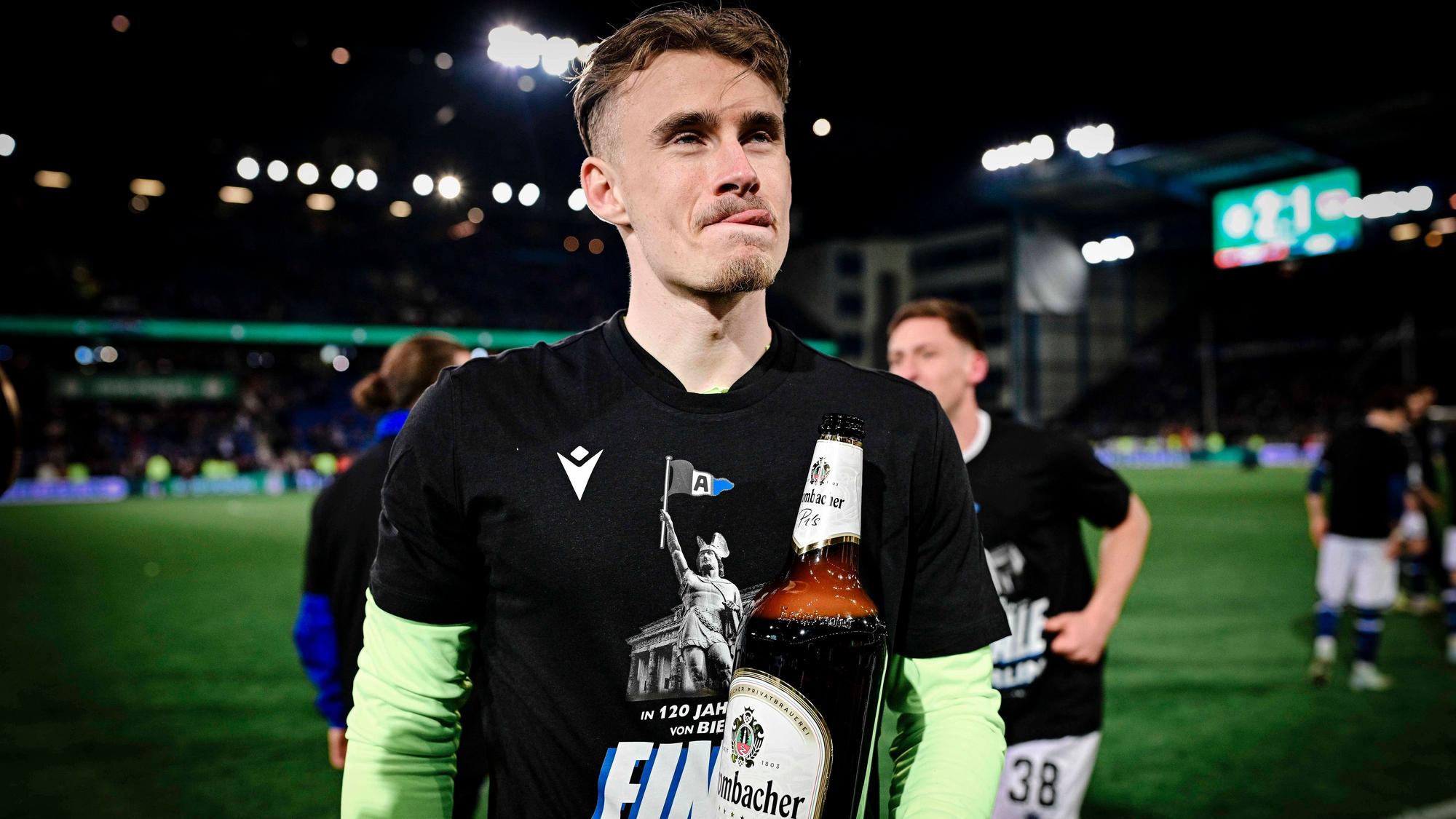 Jonas Kersken mit einer riesigen Flasche Bier in der Hand. Er leckt sich die Lippen.