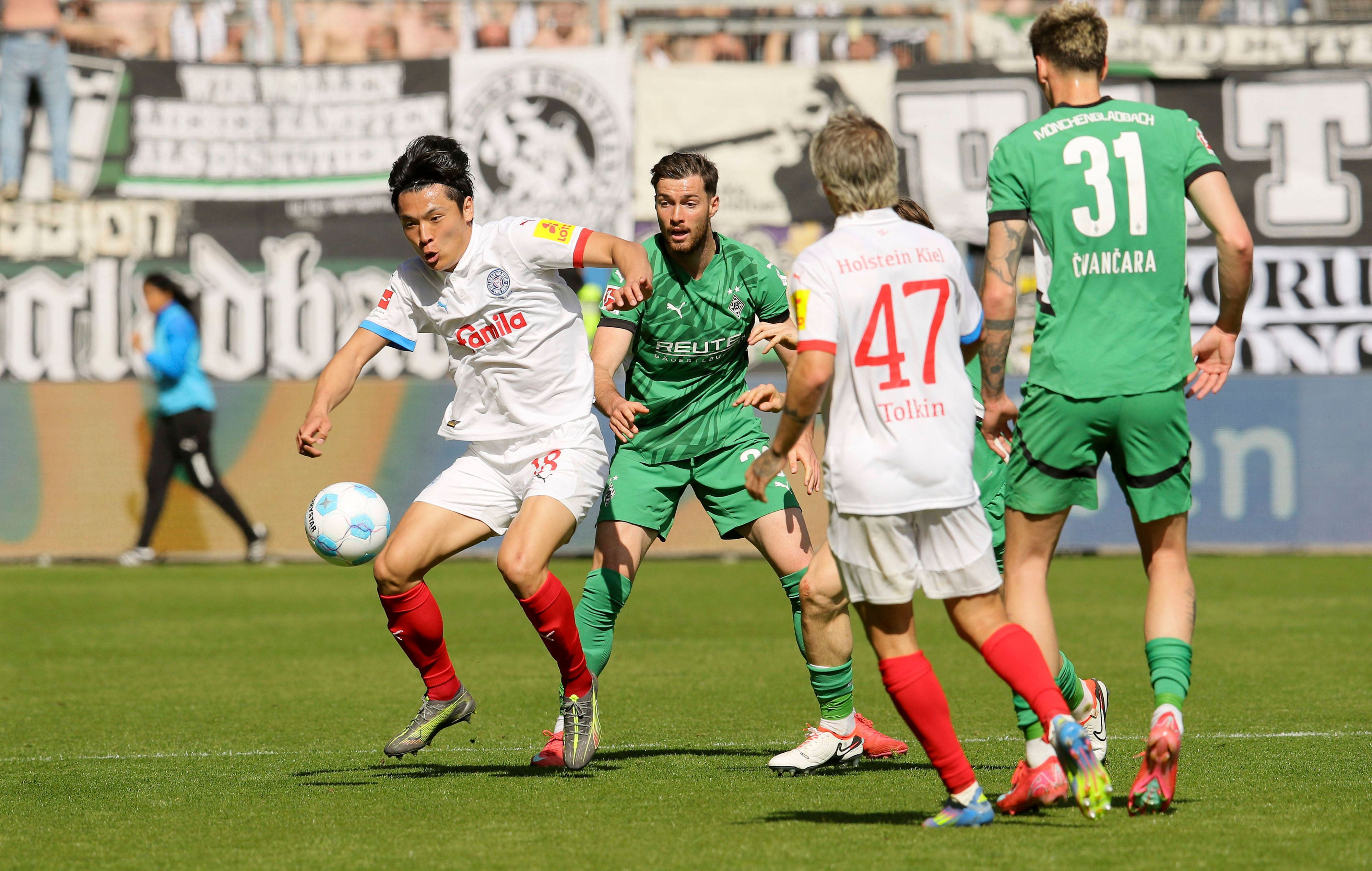 Kiels Shuto Machino spielt den Ball. Ebenfalls zu sehen: Gladbachs Joe Scally, Tomas Cvancara und Kiels John Tolkin.