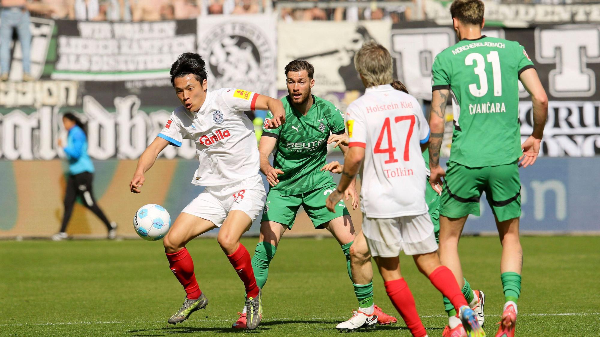 Kiels Shuto Machino spielt den Ball. Ebenfalls zu sehen: Gladbachs Joe Scally, Tomas Cvancara und Kiels John Tolkin.