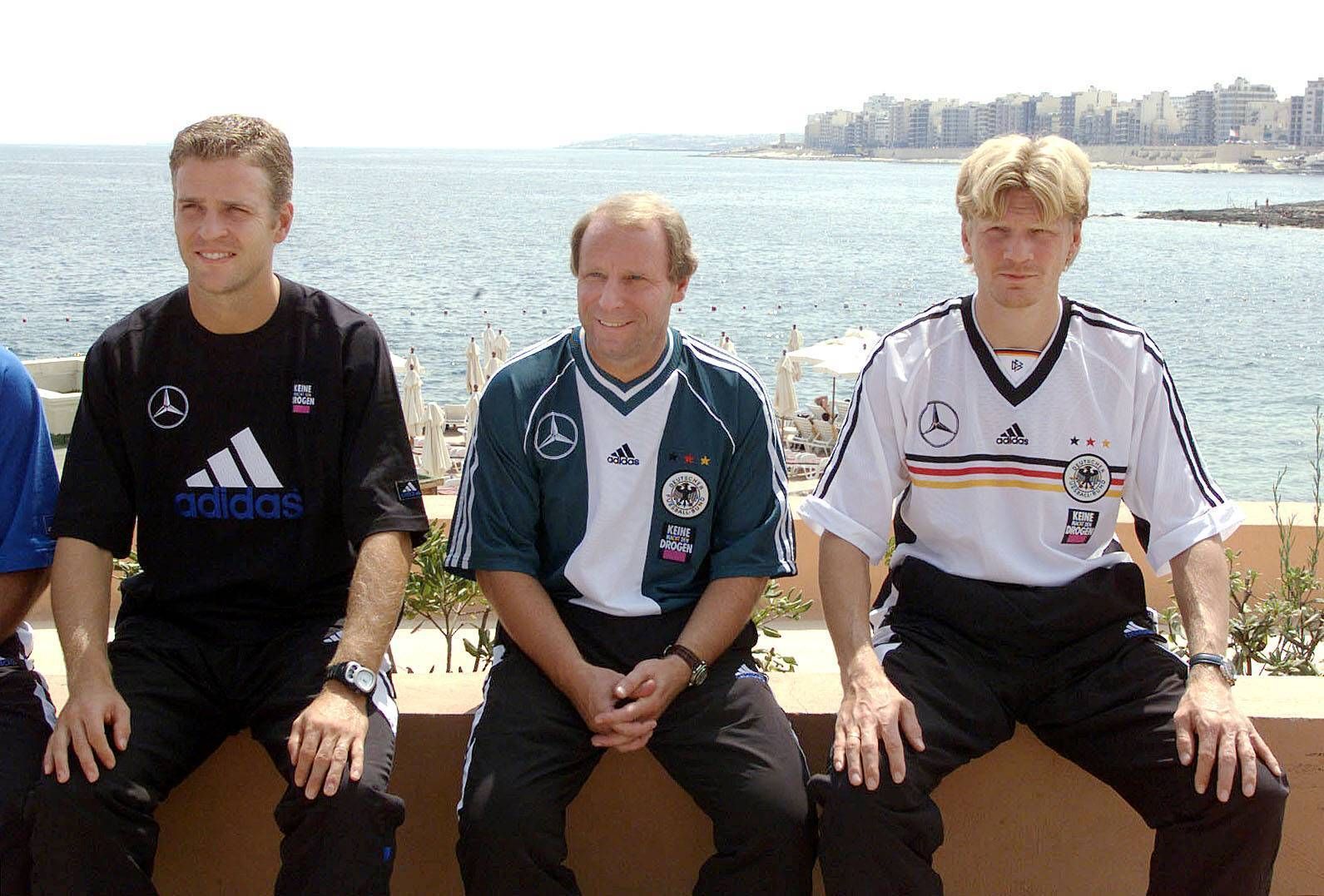 Oliver Bierhoff, Berti Vogts und Stefan Effenberg sitzen in DFB-Klamotten am Meer.