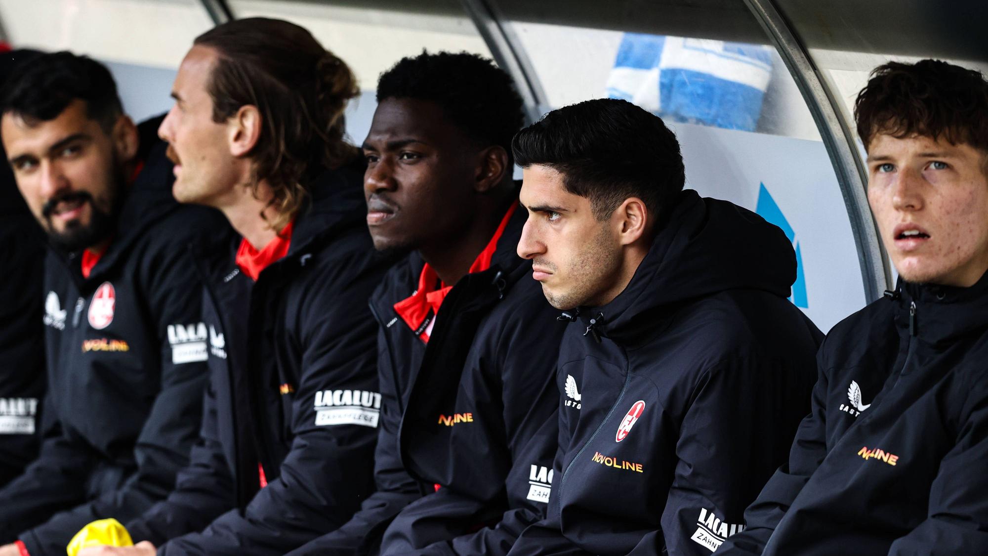 Faride Alidou und Grant Leon Ranos vom 1. FC Kaiserslautern sitzen neben ihren Teamkollegen auf der Ersatzbank.