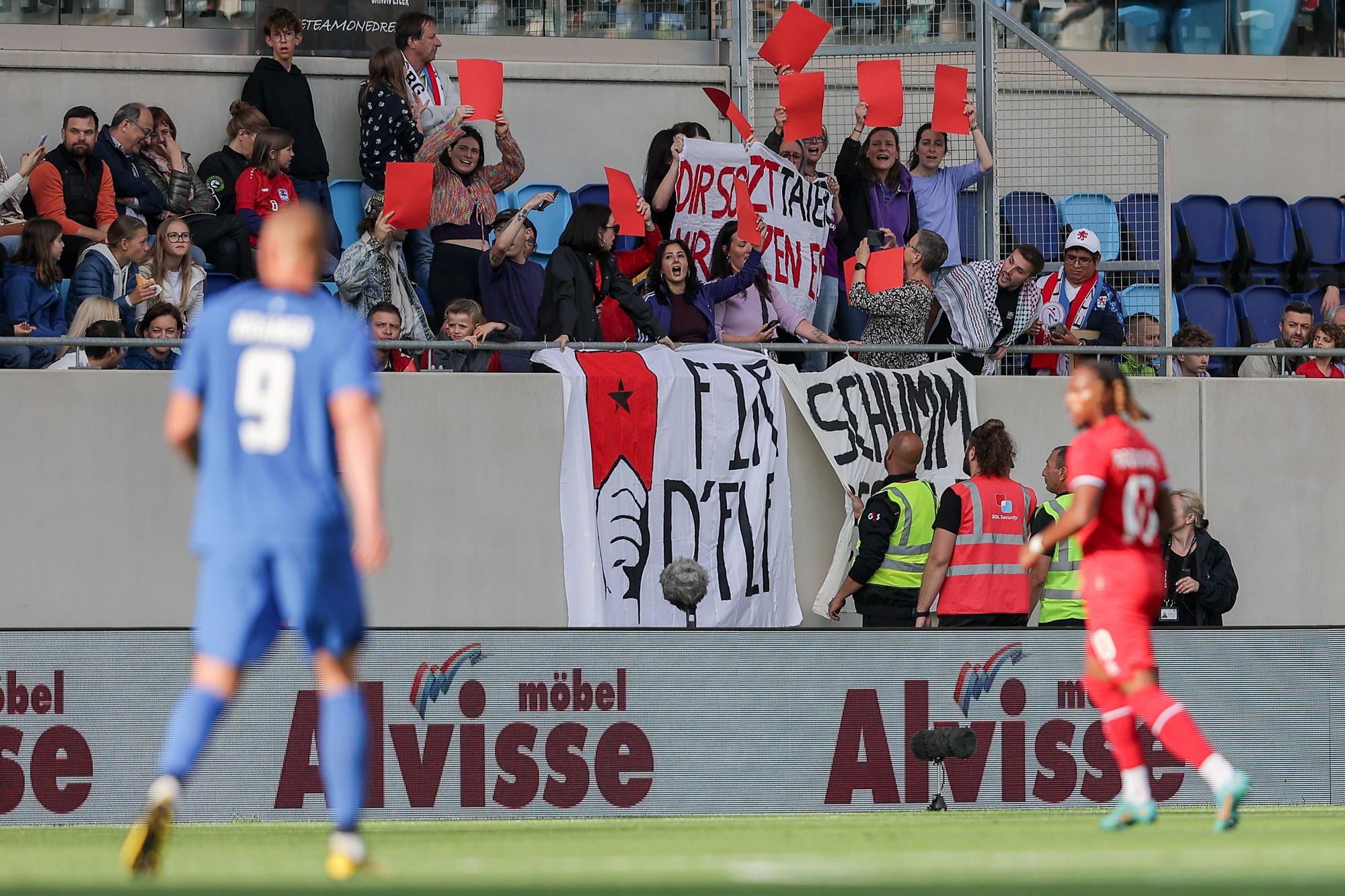 Fans protestieren mit Bannern, auf denen steht „Rote Karte für die FLF“ und „Schäm dich, FLF“.