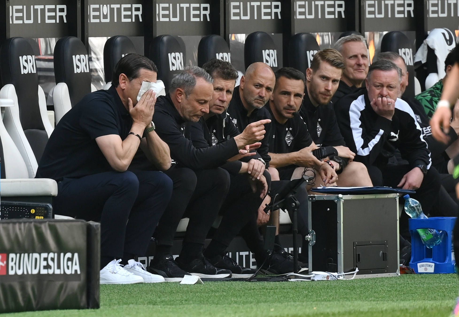 Blick auf die Bank von Borussia Mönchengladbach: Trainer Gerardo Seoane vergräbt sein Gesicht in einem Taschentuch, Roland Virkus schaut konzentriert auf das Spielfeld.