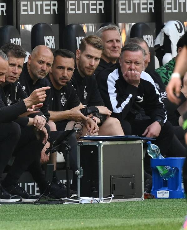 Blick auf die Bank von Borussia Mönchengladbach: Trainer Gerardo Seoane vergräbt sein Gesicht in einem Taschentuch, Roland Virkus schaut konzentriert auf das Spielfeld.
