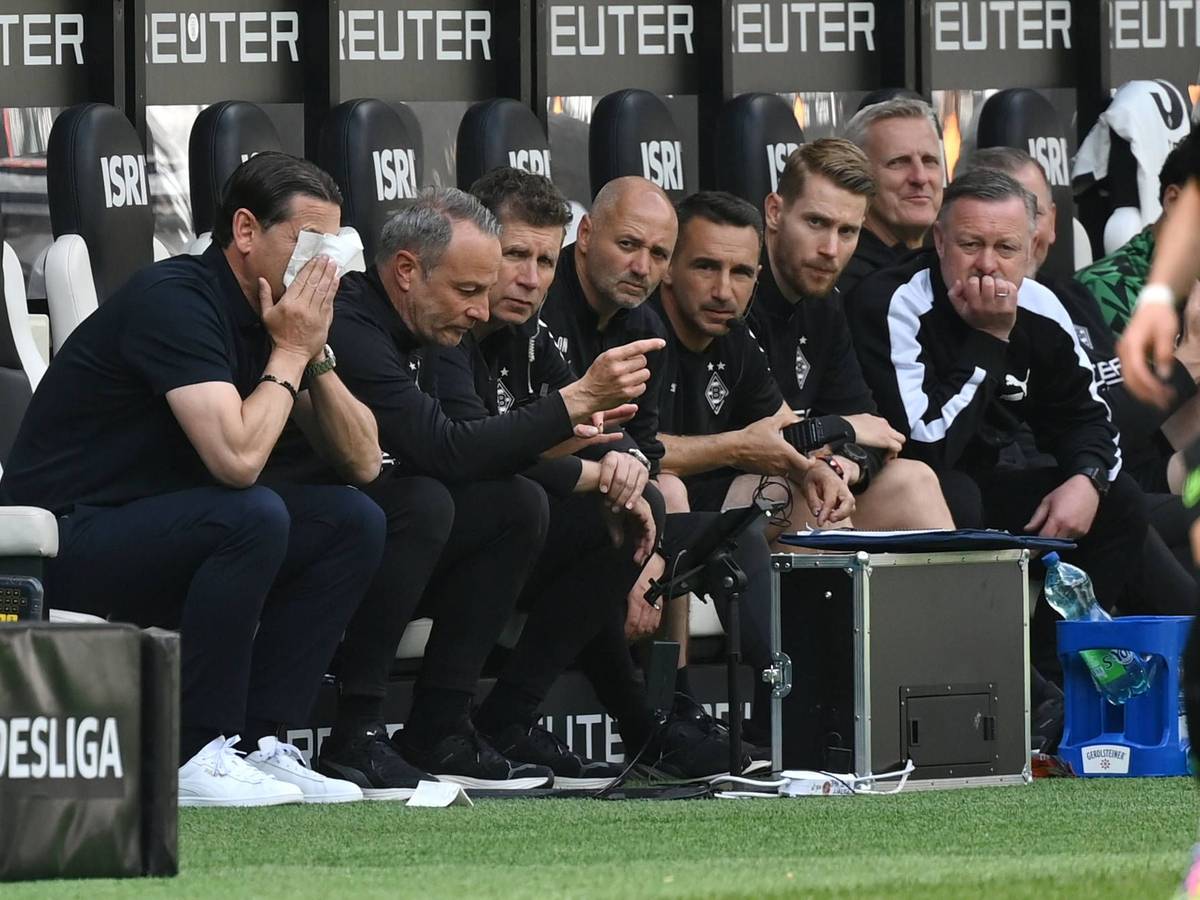 Blick auf die Bank von Borussia Mönchengladbach: Trainer Gerardo Seoane vergräbt sein Gesicht in einem Taschentuch, Roland Virkus schaut konzentriert auf das Spielfeld.