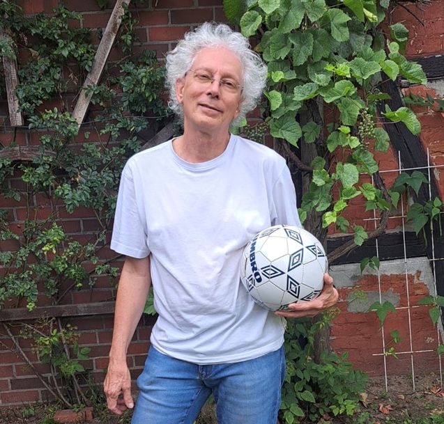 Holger Jenrich steht mit einem Ball in der Hand vor einer Hauswand.