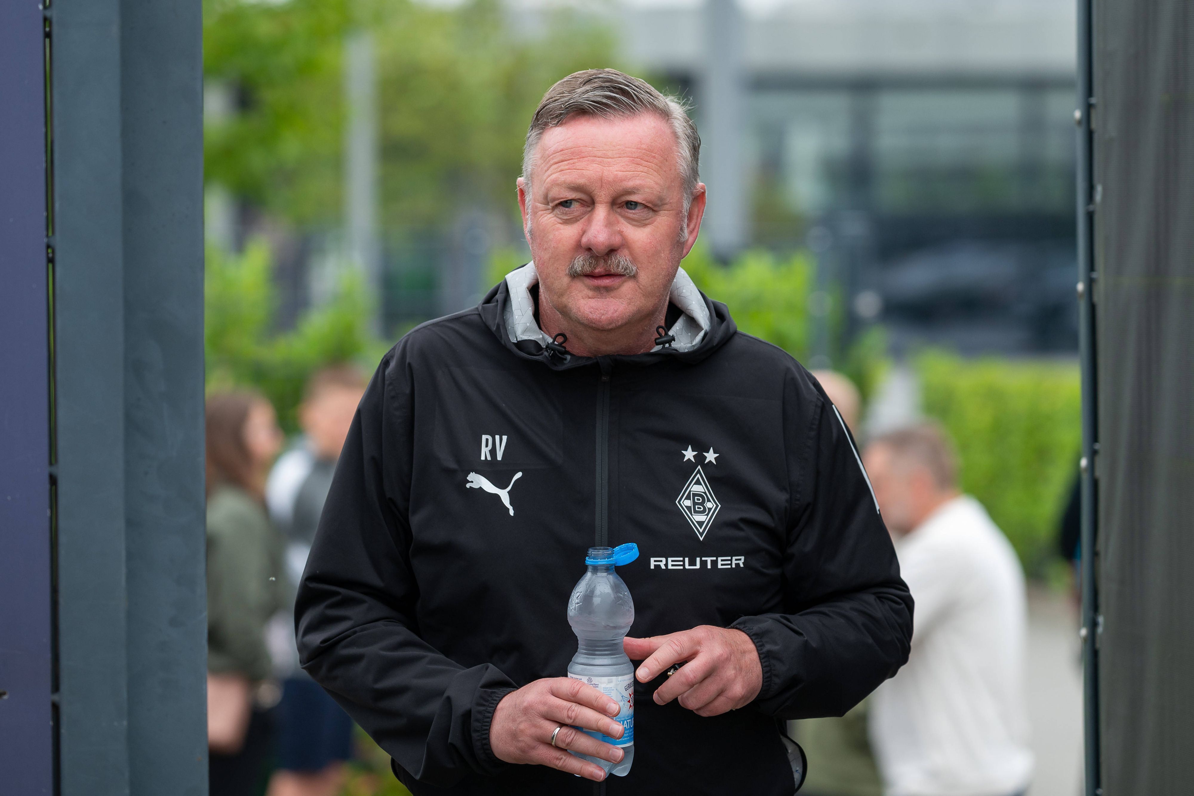 Roland Virkus betritt mit einer Wasserflasche den Trainingsplatz.