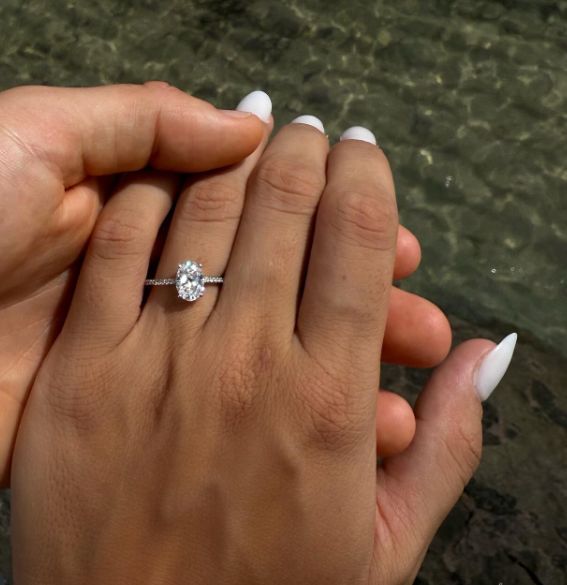 Eine Frauen-Hand mit einem Verlobungsring am Finger vor dem Meer.