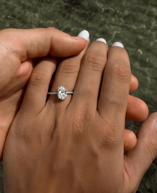 Eine Frauen-Hand mit einem Verlobungsring am Finger vor dem Meer.