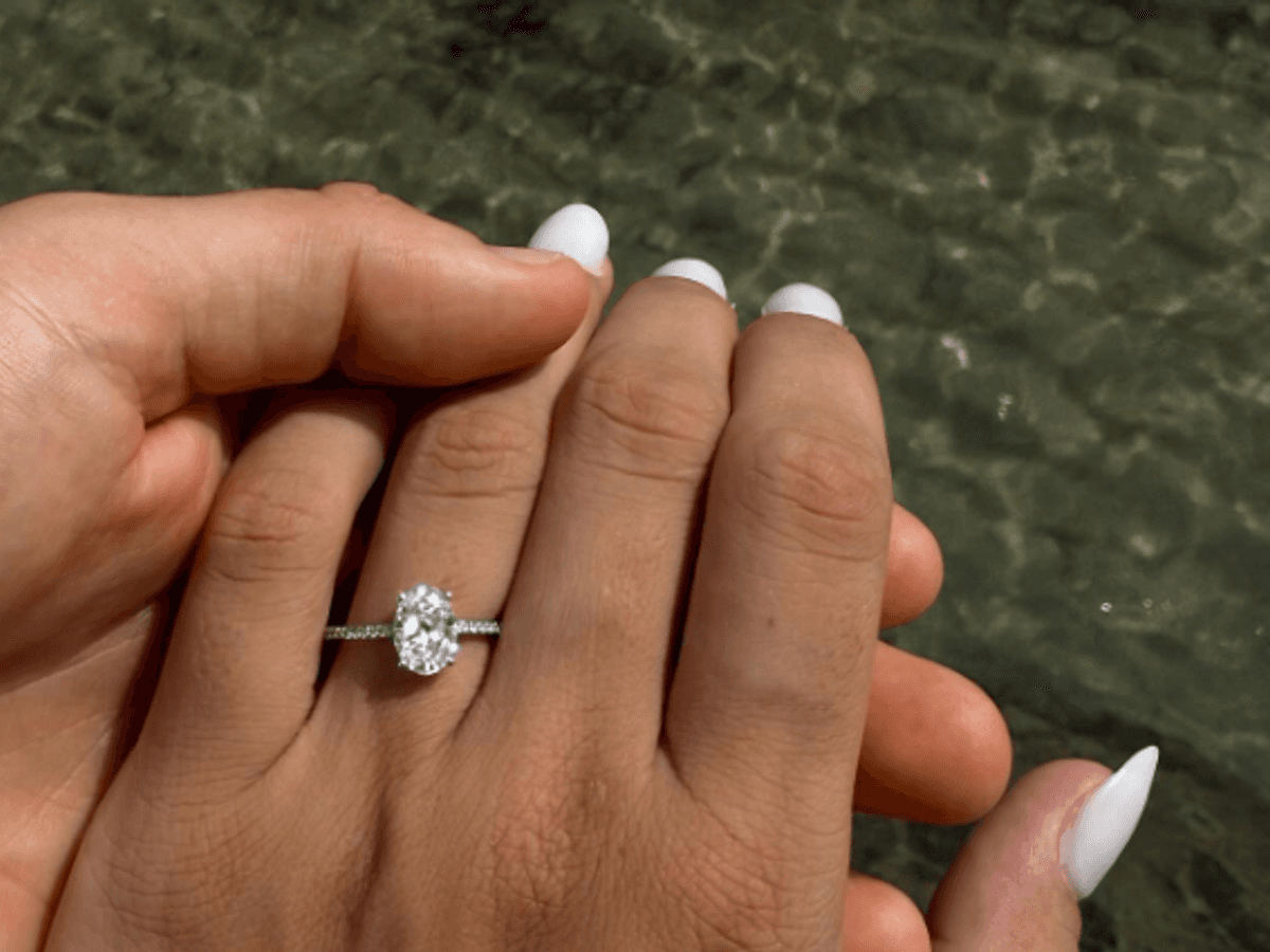 Eine Frauen-Hand mit einem Verlobungsring am Finger vor dem Meer.