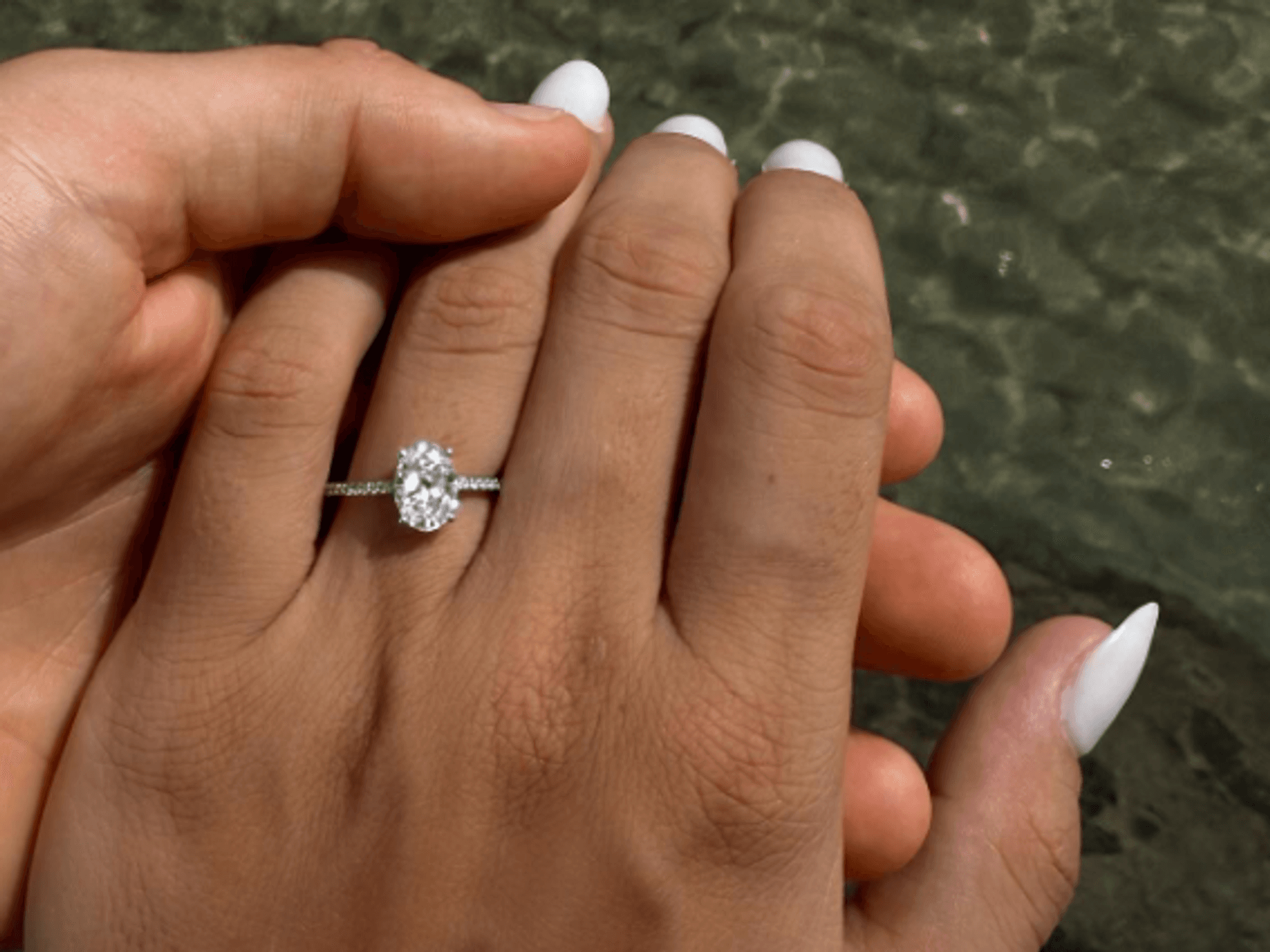 Eine Frauen-Hand mit einem Verlobungsring am Finger vor dem Meer.