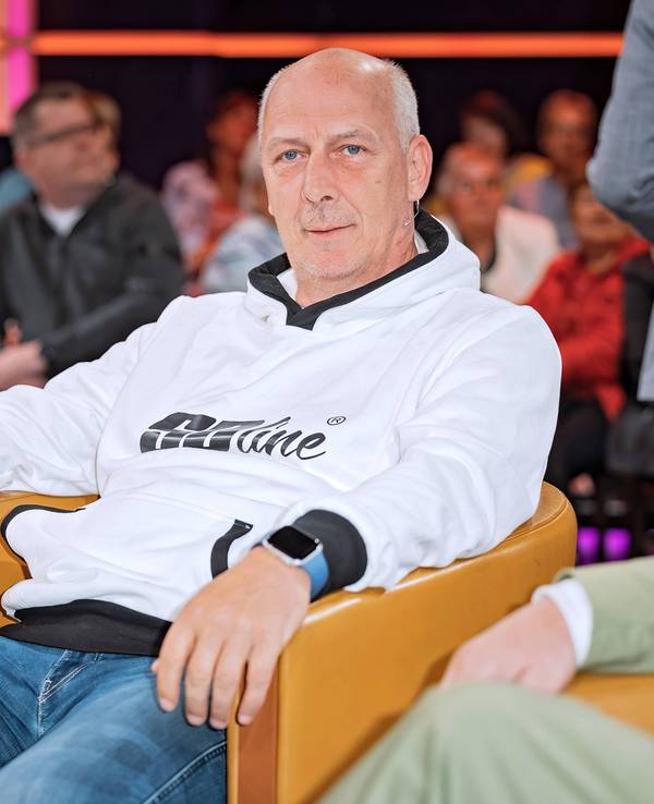 Mario Basler sitzt auf einem senffarbenen Sessel und hat beide Arme auf den Armlehnen liegen.