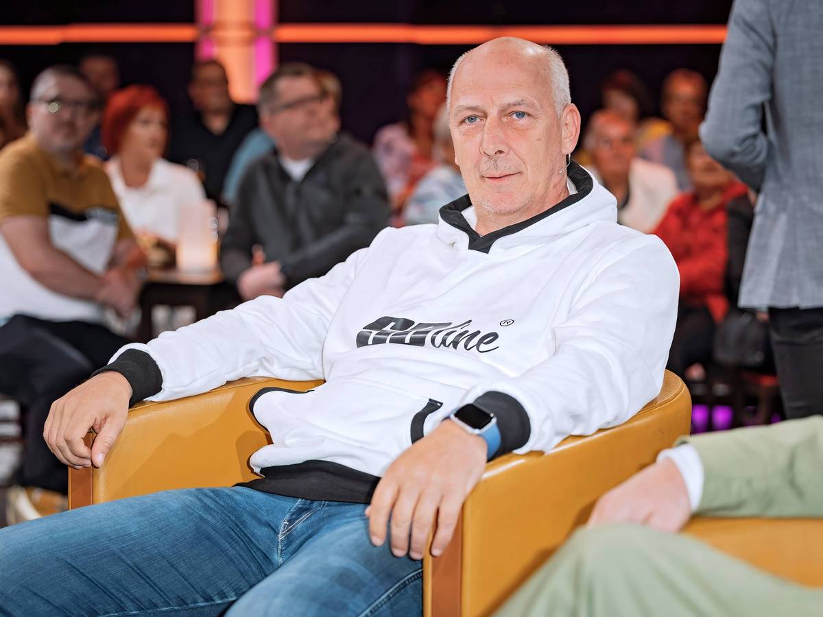 Mario Basler sitzt auf einem senffarbenen Sessel und hat beide Arme auf den Armlehnen liegen.