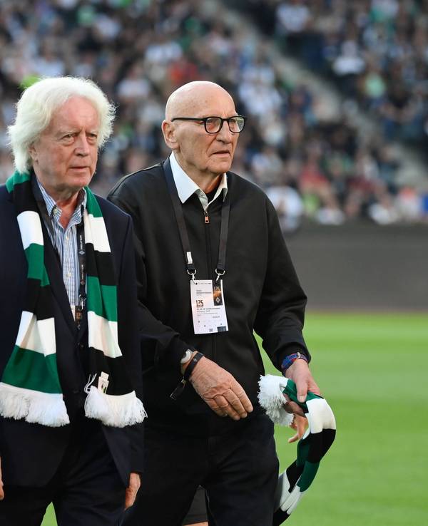 Winnie Schäfer und Wolfgang Kleff gehen bei der Jubiläumsfeier über den Rasen. Schäfer trägt einen Fanschal um den Hals, Kleff hält seinen in der linken Hand.