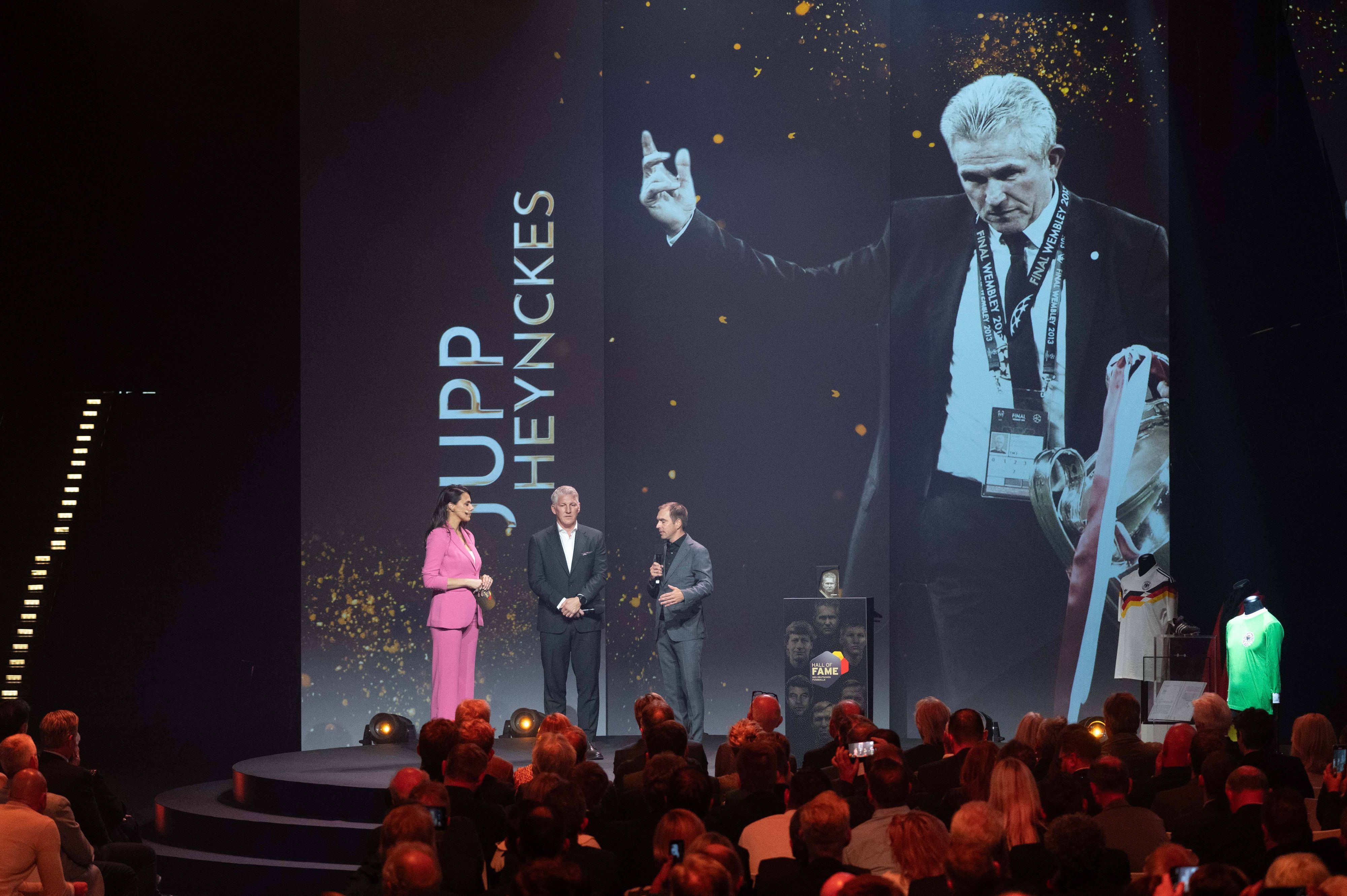 Ein Bild von Jupp Heynckes mit dem Champions-League-Pokal wird auf einer großen Leinwand gezeigt.