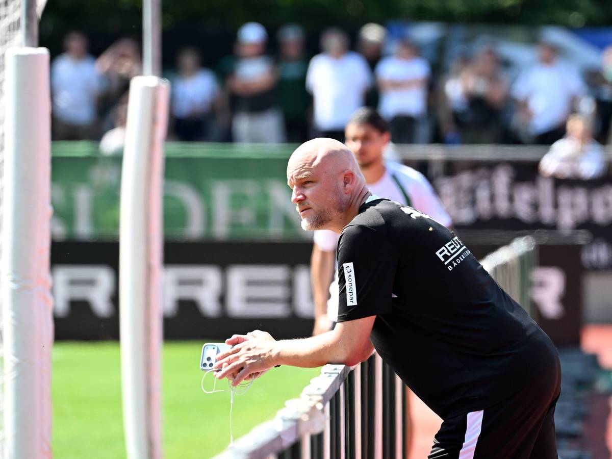 Rouven Schröder steht am Trainingsplatz und hat dabei ein Handy in der Hand.