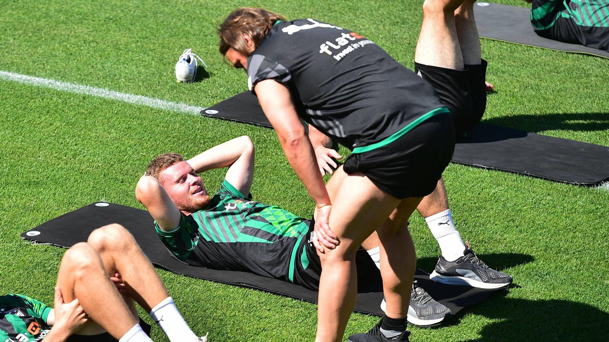 Nico Elvedi macht Gymnastikübungen auf einer Matte und Daniel Farke spricht ihm gut zu.